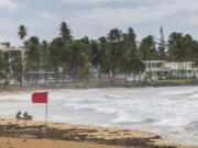 Tourists sit on La Pared beach as Tropical Storm Ernesto passes by Luquillo, Puerto Rico, Tuesday, Aug. 13, 2024.