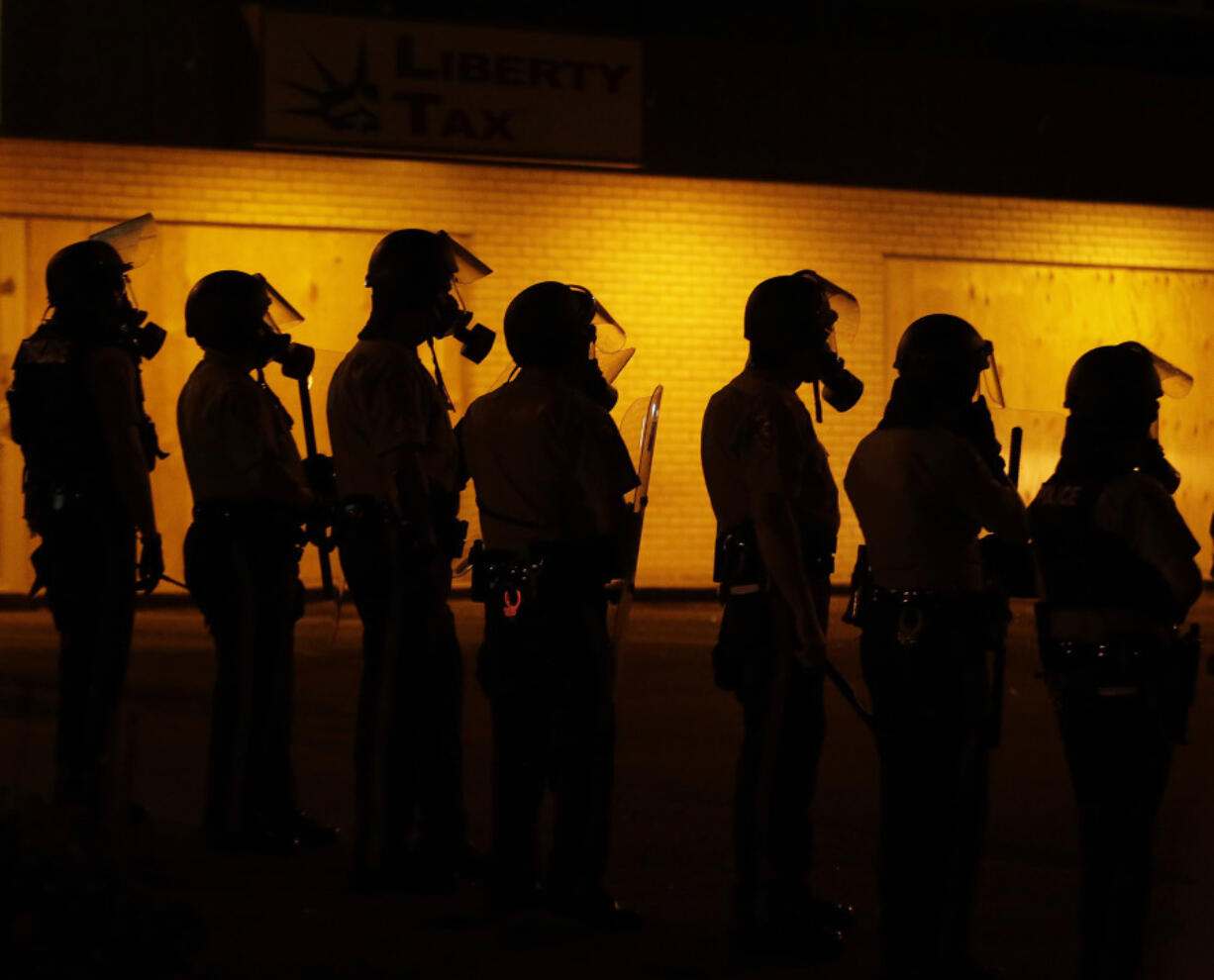 FILE - Police wait to advance after tear gas was used to disperse a crowd during protests against the shooting death of Michael Brown Jr. on Aug. 17, 2014 in Ferguson, Mo.