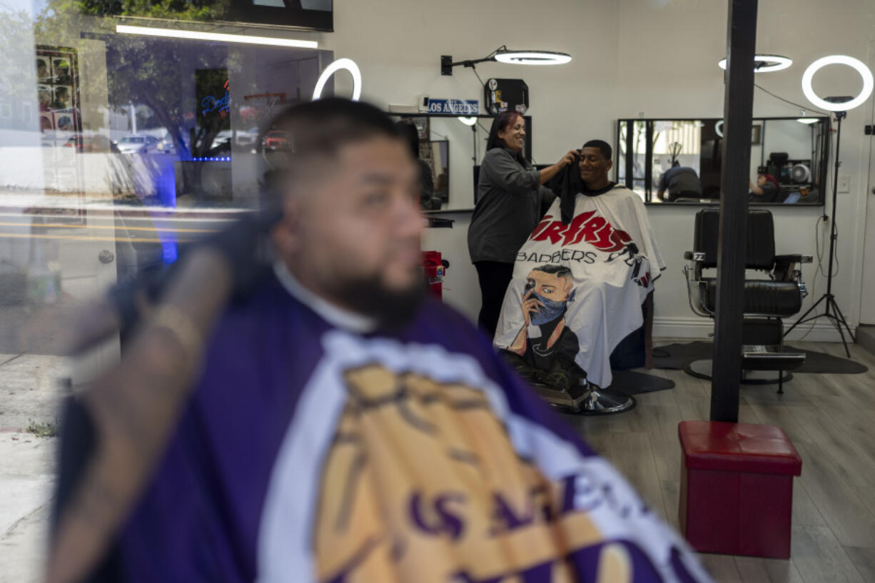 Adelita Valentine, owner of HairFreek Barbers, uses a towel to wipe away hair from the face of Cameron Loualhati in Los Angeles, Wednesday, Aug. 21, 2024. (AP Photo/Jae C.