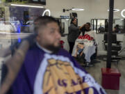 Adelita Valentine, owner of HairFreek Barbers, uses a towel to wipe away hair from the face of Cameron Loualhati in Los Angeles, Wednesday, Aug. 21, 2024. (AP Photo/Jae C.