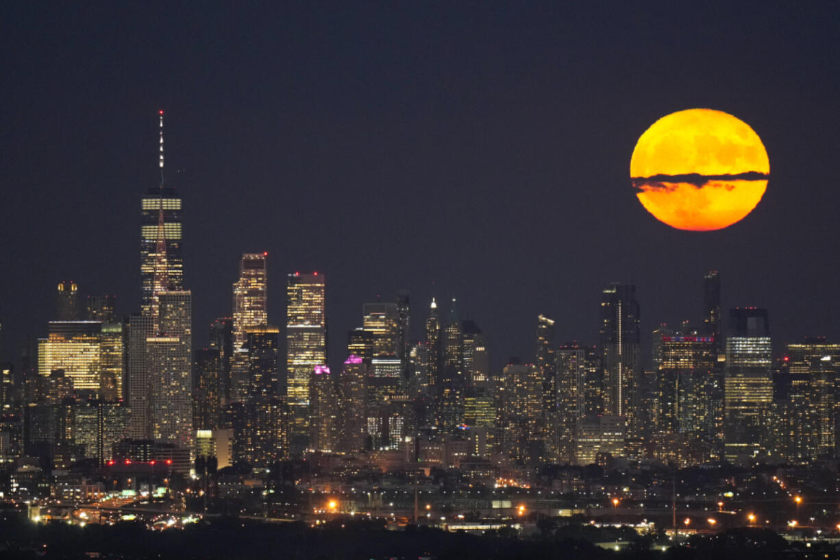 The moon rises Aug. 1, 2023, through clouds over the skyline of Lower Manhattan in this view from West Orange, N.J.