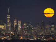 The moon rises Aug. 1, 2023, through clouds over the skyline of Lower Manhattan in this view from West Orange, N.J.