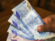 A vendor holds a handful of Trinidad and Tobago dollars, in Port-of-Spain, Trinidad and Tobago, Tuesday, Aug. 20, 2024. Prime Minister Keith Rowley announced Sunday, Aug. 18, 2024, the country is redrawing the island&rsquo;s coat of arms to remove references to European colonization and that Christopher Columbus&rsquo; three ships will be replaced with the steelpan, a popular percussion instrument.