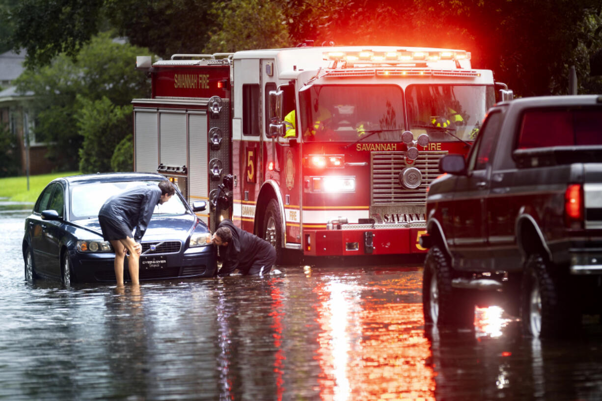 People attach a towline to a stranded vehicle on a flooded street after heavy rain from Tropical Storm Debby, Monday, Aug. 5, 2024, in Savannah, Ga. (AP Photo/Stephen B.