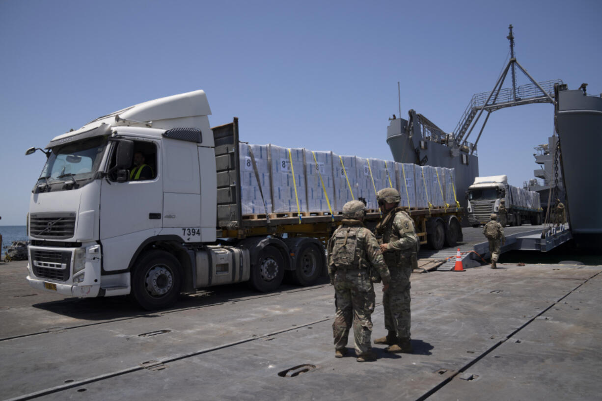 FILE - U.S. Army soldiers stand next to trucks arriving loaded with humanitarian aid at the U.S.-built floating pier Trident before reaching the beach on the coast of the Gaza Strip, June 25, 2024.