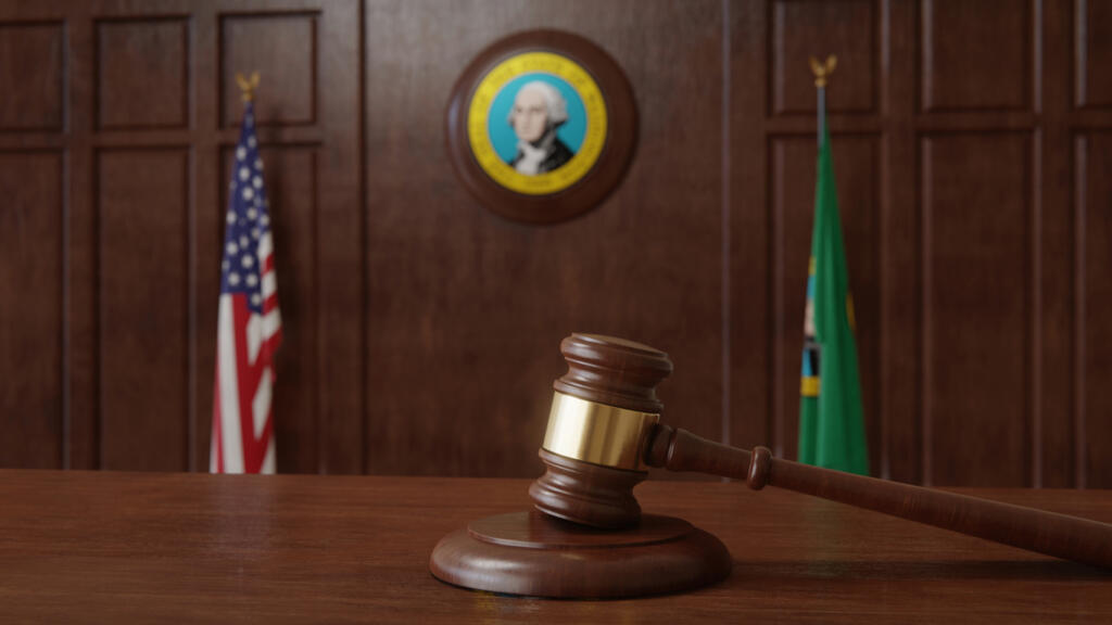 Courtroom scene with US flag and state seal and flag of the state of Washington.