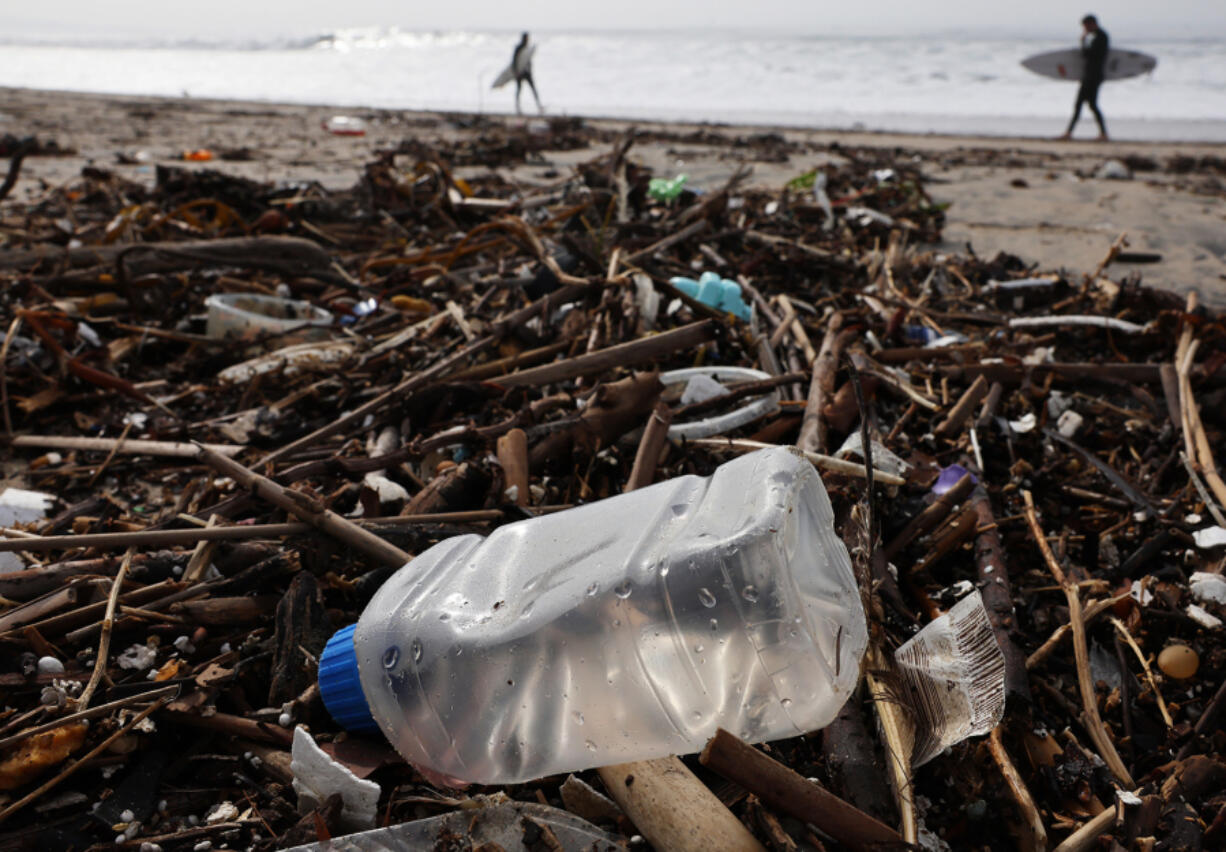 Surfers walk near debris, including a plastic bottle, washed up on the beach Dec. 29 in El Segundo, Calif.