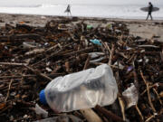 Surfers walk near debris, including a plastic bottle, washed up on the beach Dec. 29 in El Segundo, Calif.