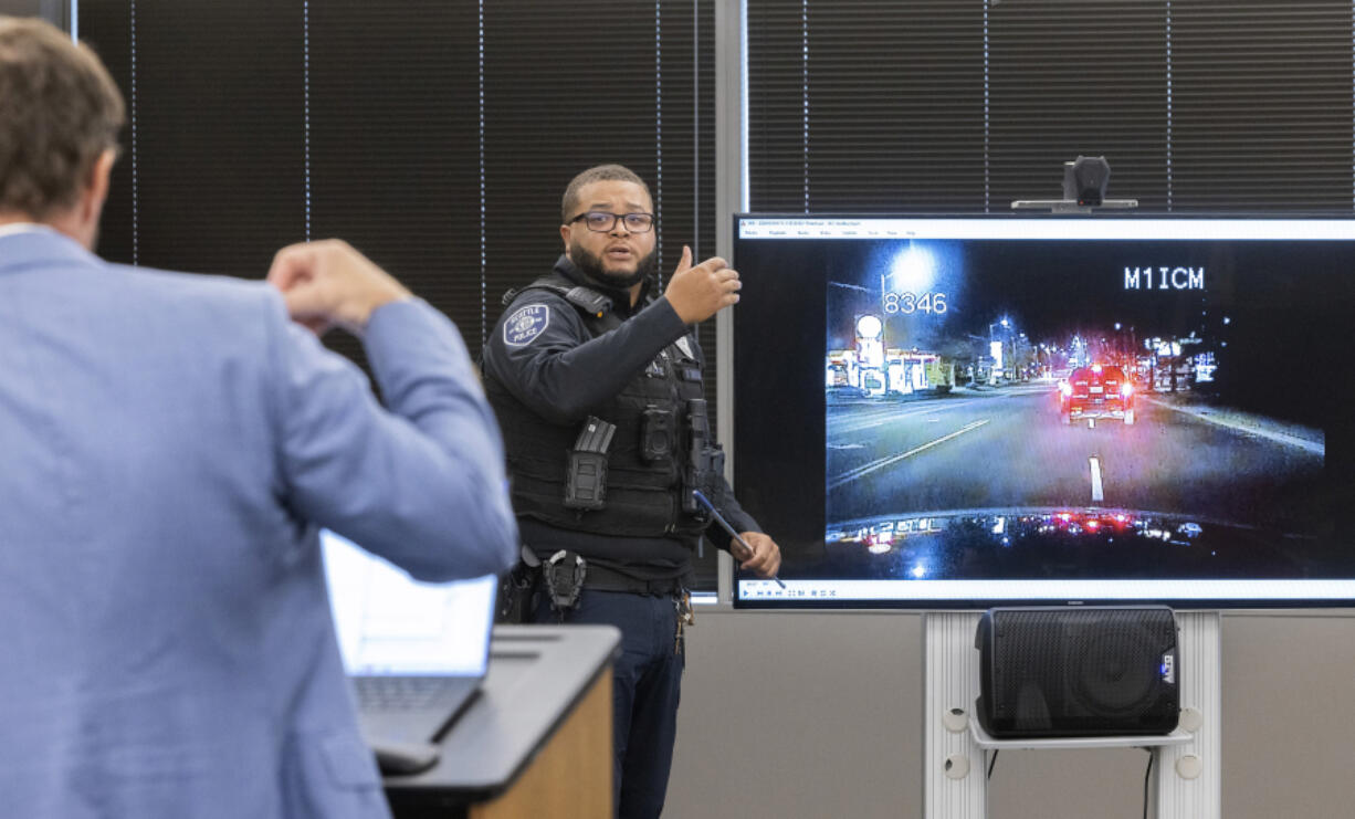 Attorney Matt Anderson, left, questions Seattle Police Officer Domisi Thrash during an inquest regarding the death of Kyle Gray Wednesday, Sept. 11, 2024, in the Chinook Building in Seattle. Gray was killed in December of 2017 and the inquest is finally taking place.  On the screen is dashboard footage from Officer Thrash&rsquo;s car when he was following Gray after a robbery. (Ellen M.