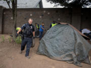 Vancouver police Cpl. Sean Metevia, left, joins cleanup crews and members of the city of Vancouver&rsquo;s Homelessness Assistance and Resource Team on July 31 as they remove solid waste along the West Mill Plain Boulevard sound wall, with a house just beyond. Residents on the other side of the sound wall want the camp cleared.