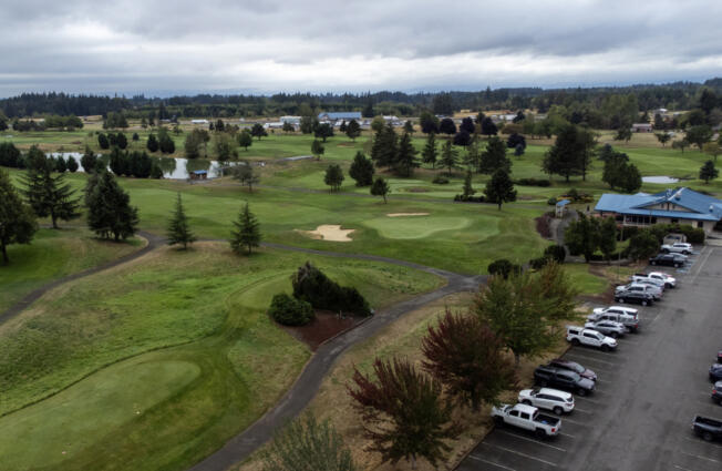 Cars sit in a parking lot next to the green Wednesday at Tri-Mountain Golf Course in Ridgefield. Clark County is putting the course up for sale later this month.