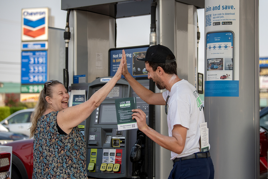 Vancouver resident DeAnna Hathaway, left, shares a high-five with Tim Lussier of Clackamas, Ore., on Friday morning. Let&rsquo;s Go Washington hosted three gas station events to highlight the Initiative 2117 campaign to repeal the state&rsquo;s Climate Commitment Act.