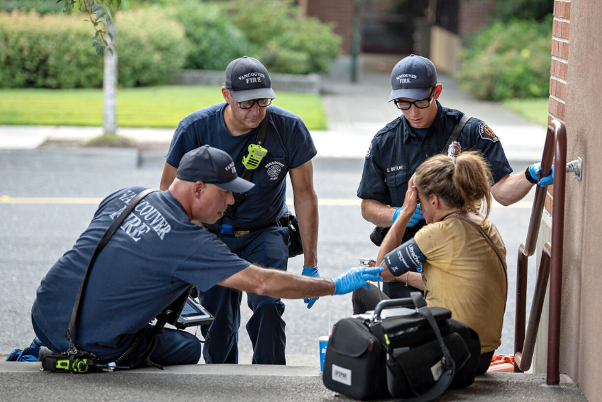 Jesse Martin, public information officer for the Vancouver Fire Department, from left, joins firefighter/engineer Paul Coulimore and firefighter/paramedic Caleb Butler as they assist a woman struggling during an excessive heat warning in Vancouver&rsquo;s Uptown Village on Thursday afternoon. The temperature was hovering near triple digits at the time of the call.