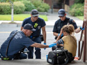 Jesse Martin, public information officer for the Vancouver Fire Department, from left, joins firefighter/engineer Paul Coulimore and firefighter/paramedic Caleb Butler as they assist a woman struggling during an excessive heat warning in Vancouver&rsquo;s Uptown Village on Thursday afternoon. The temperature was hovering near triple digits at the time of the call.