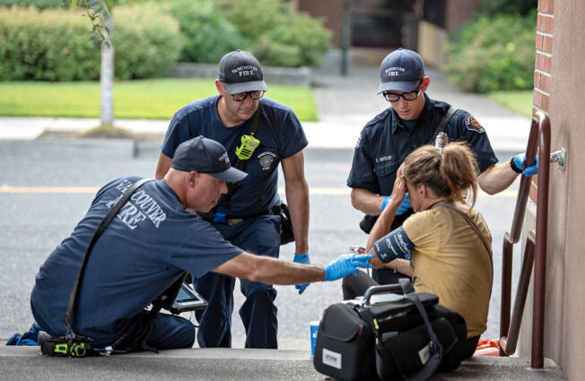 Jesse Martin, public information officer for the Vancouver Fire Department, from left, joins firefighter/engineer Paul Coulimore and firefighter/paramedic Caleb Butler as they assist a woman struggling during an excessive heat warning in Vancouver&rsquo;s Uptown Village on Thursday afternoon. The temperature was hovering near triple digits at the time of the call.