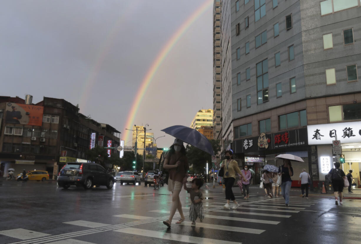 People walk in the rain with a backdrop of the rainbow in the sky as Typhoon Krathon approaches to Taiwan in Taipei, Monday, Sept. 30, 2024.