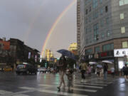 People walk in the rain with a backdrop of the rainbow in the sky as Typhoon Krathon approaches to Taiwan in Taipei, Monday, Sept. 30, 2024.