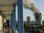 FILE - A resident in a nearby building watches smoke rise from the Grenfell Tower building on fire in London, Wednesday, June 14, 2017.