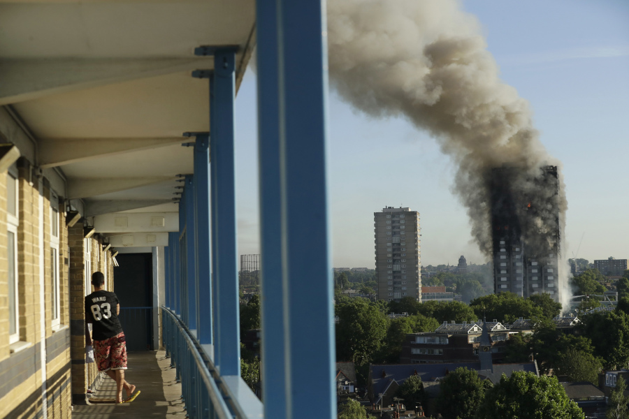 FILE - A resident in a nearby building watches smoke rise from the Grenfell Tower building on fire in London, Wednesday, June 14, 2017.