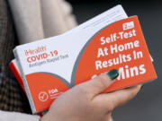 FILE - A woman holds two boxes of at-home Covid-19 test kits in Washington, Dec. 22, 2021.