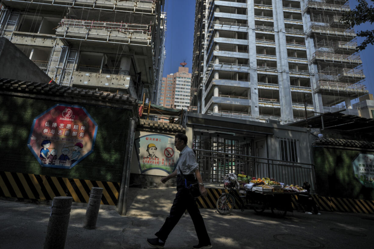 A man walks by a fruits vendor waiting for customers outside a luxury housing construction site in Beijing, Tuesday, Sept. 24, 2024.