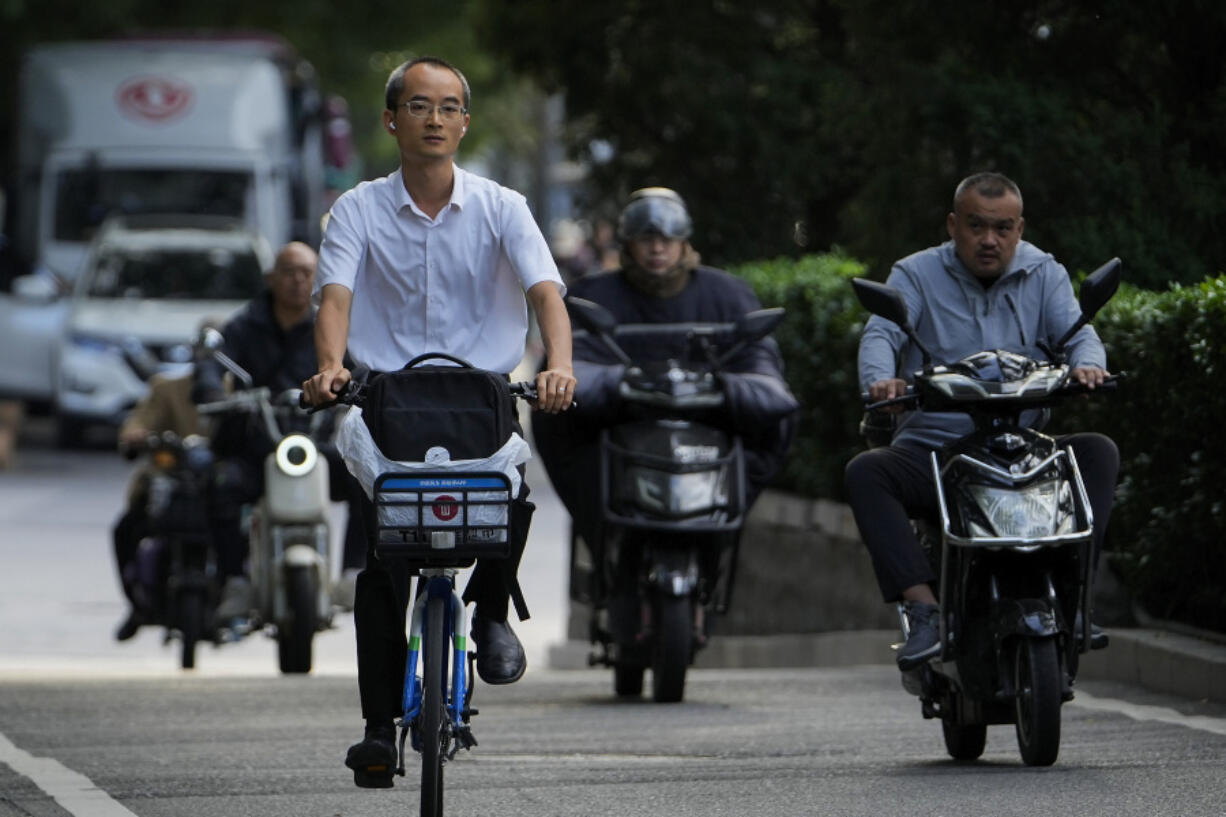 A man rides along motorists as they head to work during the morning rush hour in Beijing, Friday, Sept. 13, 2024.