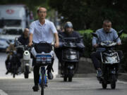 A man rides along motorists as they head to work during the morning rush hour in Beijing, Friday, Sept. 13, 2024.