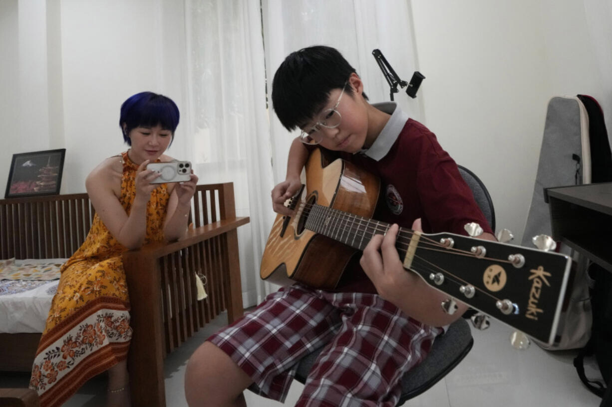 Chinese mother Jiang Wenhui, left, records her son Rodney Feng playing the acoustic guitar in Chiang Mai province, Thailand, Tuesday, April 23, 2024.(AP Photo/Sakchai Lalit)