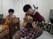 Chinese mother Jiang Wenhui, left, records her son Rodney Feng playing the acoustic guitar in Chiang Mai province, Thailand, Tuesday, April 23, 2024.(AP Photo/Sakchai Lalit)