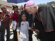 El Paso Catholic Bishop Mark Seitz talks with Celsia Palma, 9, of Honduras, as they walked June 27, 2019, to the Paso Del Norte International Port of Entry in Juarez, Mexico.