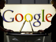 In this April 17, 2007 file photo, exhibitors work on laptop computers in front of an illuminated sign of the Google logo at the industrial fair Hannover Messe in Hanover, Germany.