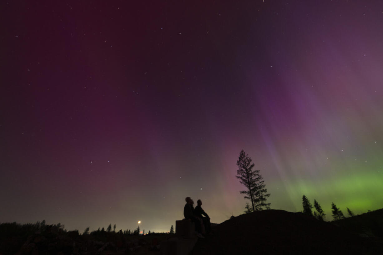 FILE - In this image taken with a long exposure, people look at the night sky towards the northern lights, or Aurora Borealis, May 10, 2024, in Estacada, Ore.