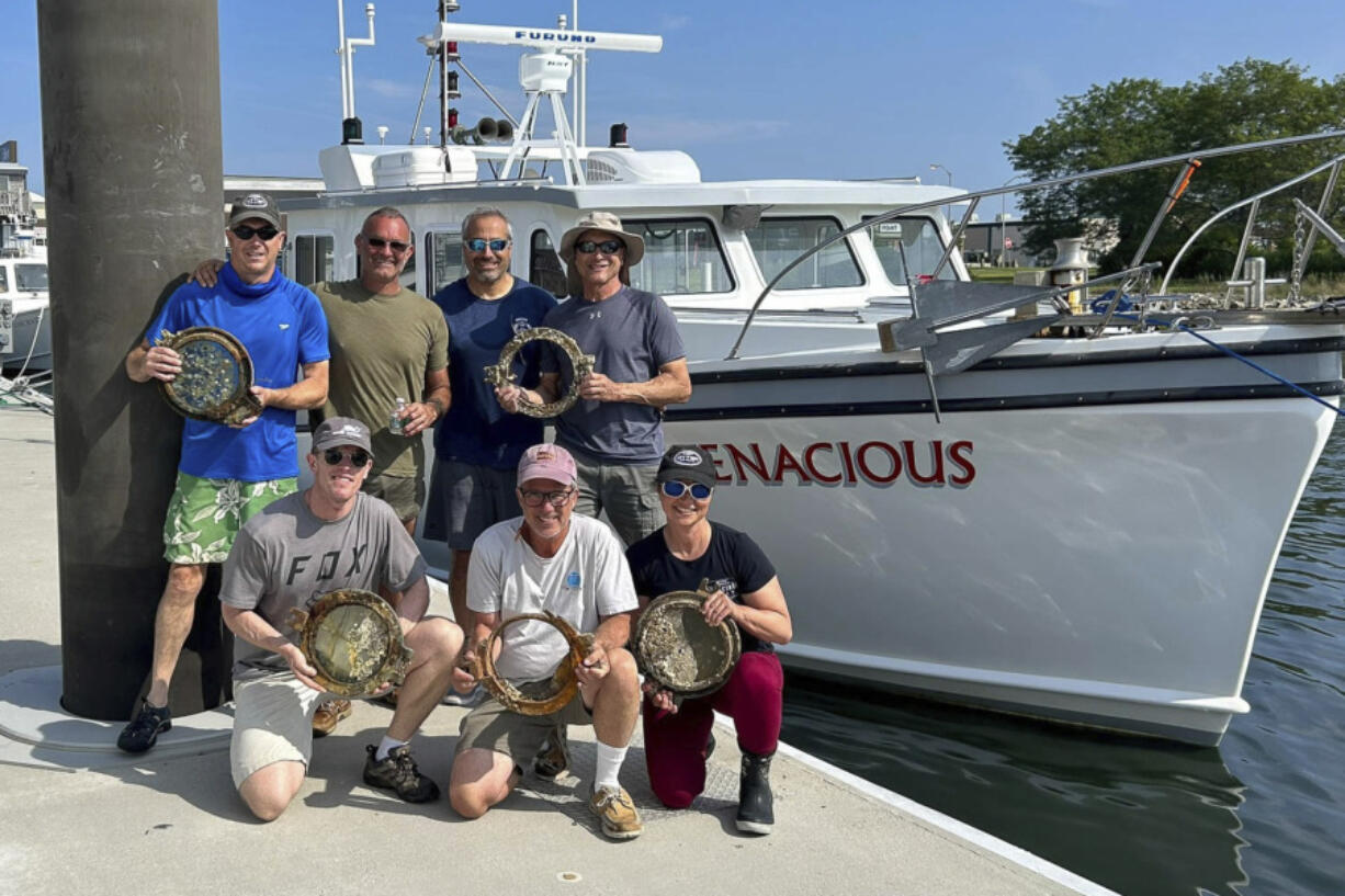 In this undated photo provided by Atlantic Wreck Salvage, members the Discovery team pose in New Bedford, Mass., on Sunday, Aug. 25, 2024. with portholes recovered from the passenger steamship Le Lyonnais.