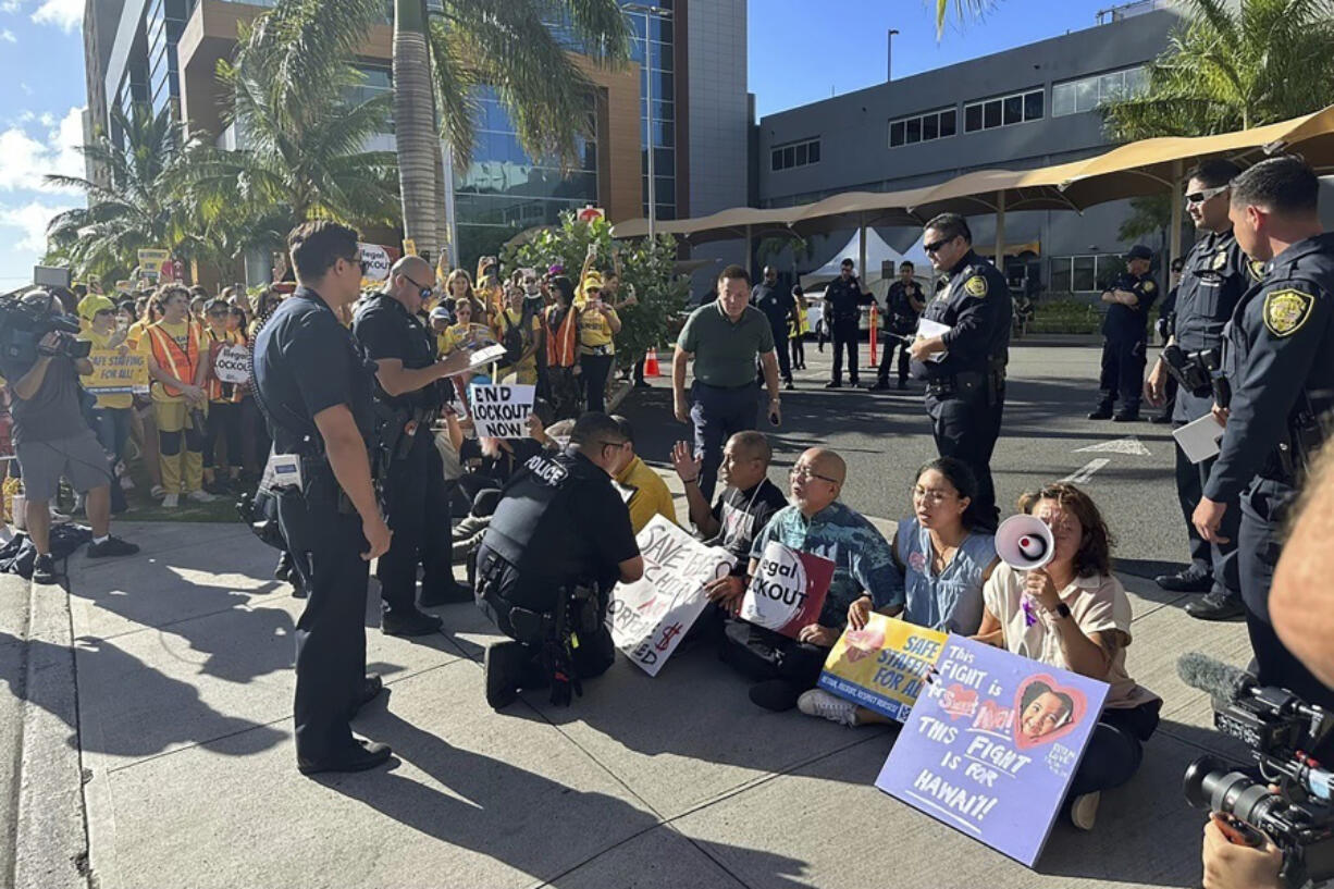 In this photo provided by Ashley Young, Honolulu police officers talk to demonstrators sitting outside a medical center in Honolulu, Monday, Sept. 23, 2024, where unionized nurses have been locked out since going on a one-day strike.