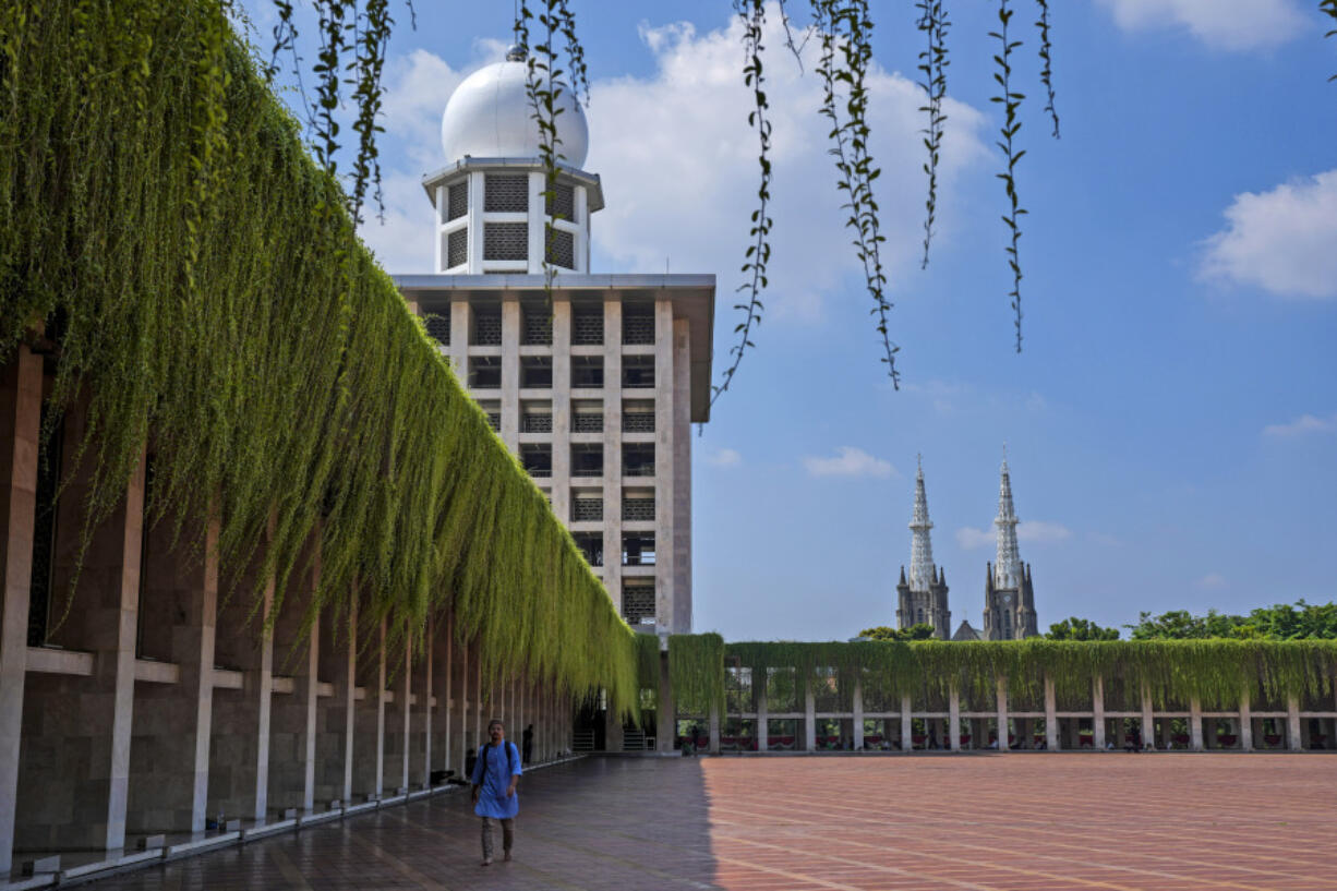 A man walks in the shade at Istiqlal Mosque as the spires of the Our Lady of The Assumption Cathedral are seen in the background, in Jakarta, Indonesia, Friday, Aug. 9, 2024.