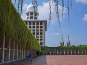 A man walks in the shade at Istiqlal Mosque as the spires of the Our Lady of The Assumption Cathedral are seen in the background, in Jakarta, Indonesia, Friday, Aug. 9, 2024.