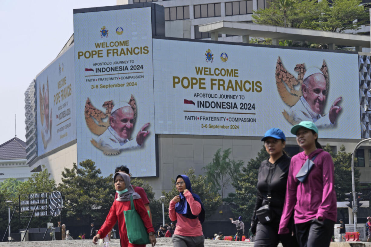 People walk past a welcoming message for Pope Francis displayed on a large digital advertisement board in Jakarta, Sunday, Sept. 1, 2024, ahead of his visit to Indonesia from Sept. 3-6.