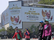 People walk past a welcoming message for Pope Francis displayed on a large digital advertisement board in Jakarta, Sunday, Sept. 1, 2024, ahead of his visit to Indonesia from Sept. 3-6.