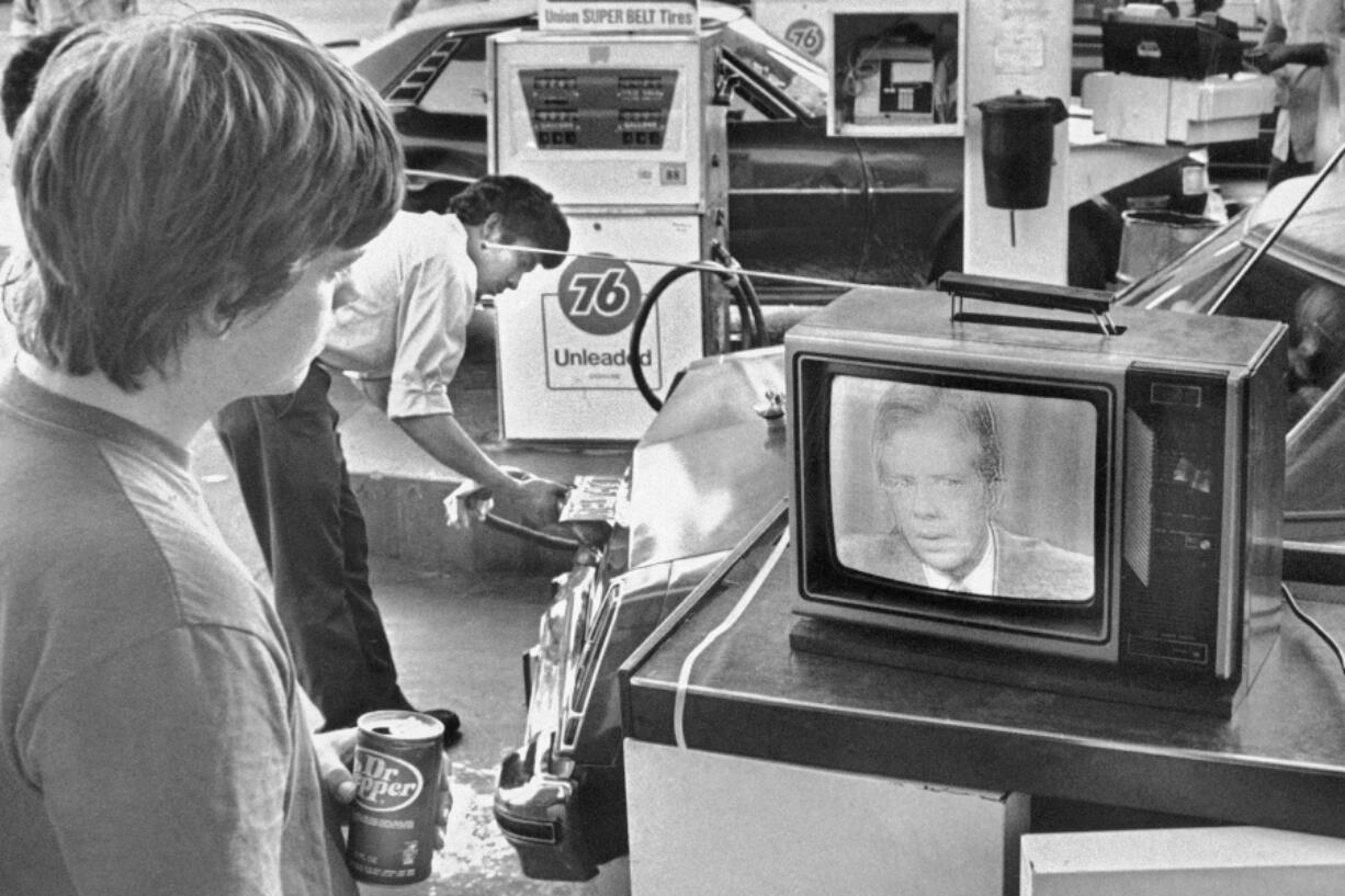 FILE - College student Chuck McManis watches President Jimmy Carter&rsquo;s nationally televised energy speech from a service station in Los Angeles, as a gas station attendant fills up a customer&rsquo;s car, July 15, 1979.