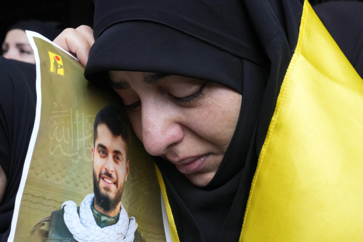 A woman holds a picture of a Hezbollah member who was killed on Wednesday when a handheld device exploded, during his funeral procession in the southern suburbs of Beirut, Thursday, Sept. 19, 2024.