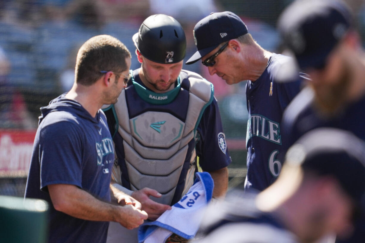 Seattle Mariners catcher Cal Raleigh, center, is checked out for injury after attempting to catch a foul ball hit by Los Angeles Angels&#039; Kevin Pillar during the eighth inning of a baseball game in Anaheim, Calif., Sunday, Sept. 1, 2024.