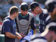 Seattle Mariners catcher Cal Raleigh, center, is checked out for injury after attempting to catch a foul ball hit by Los Angeles Angels&#039; Kevin Pillar during the eighth inning of a baseball game in Anaheim, Calif., Sunday, Sept. 1, 2024.