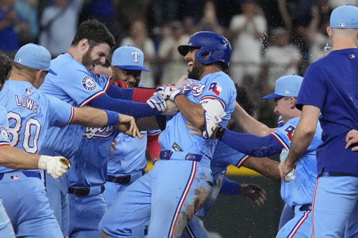 Texas Rangers&#039; Marcus Semien, center wearing a helmet, is congratulated by teammates after hitting a single that scored Leody Taveras during the ninth inning of a baseball game against the Seattle Mariners Sunday, Sept.