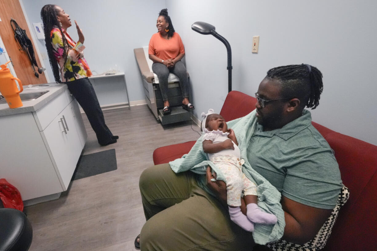 Jennie Joseph, back left, lead midwife and clinic director at the Commonsense Childbirth clinic talks with client Regine Baramore as husband Scott holds six-week-old daughter, Yahareice, Wednesday, June 26, 2024, in Orlando, Fla.