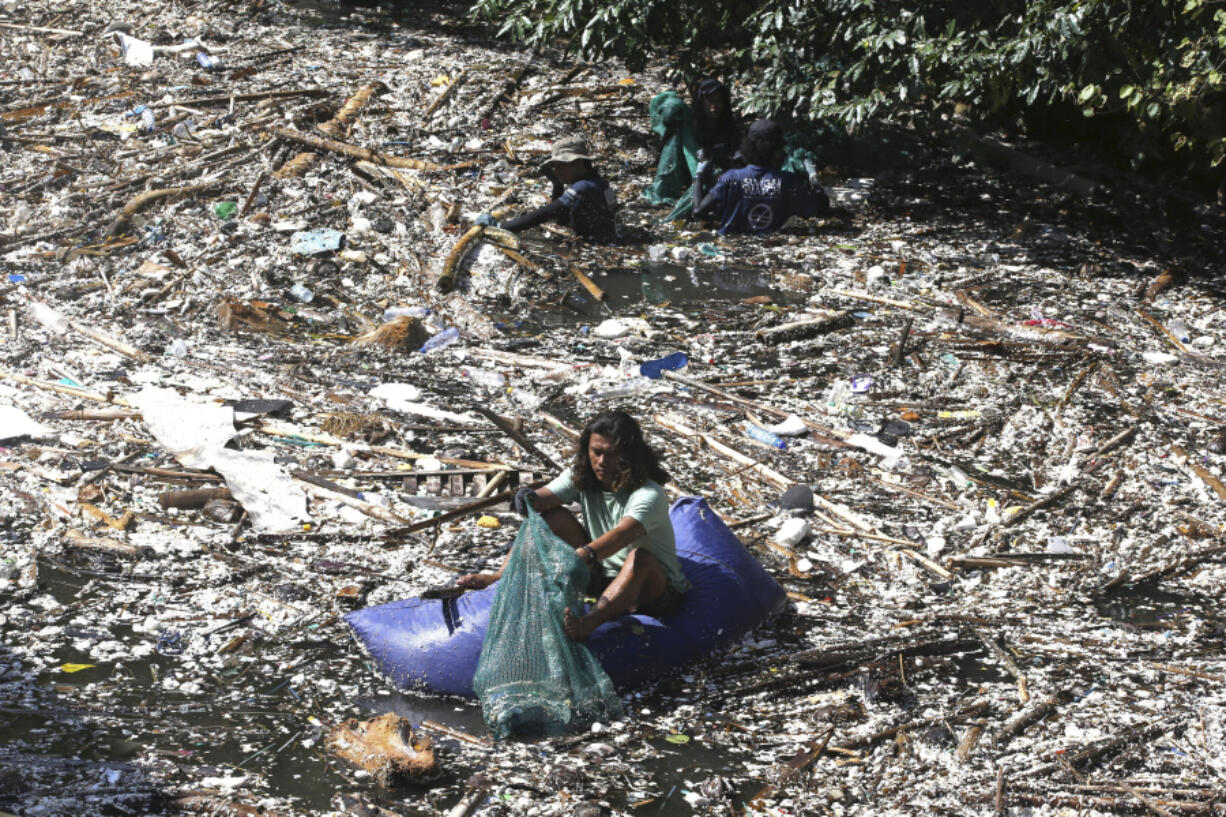 FILE - A volunteer picks up trash on a river which is covered with trash at Pecatu, Bali, Indonesia, March 22, 2024.