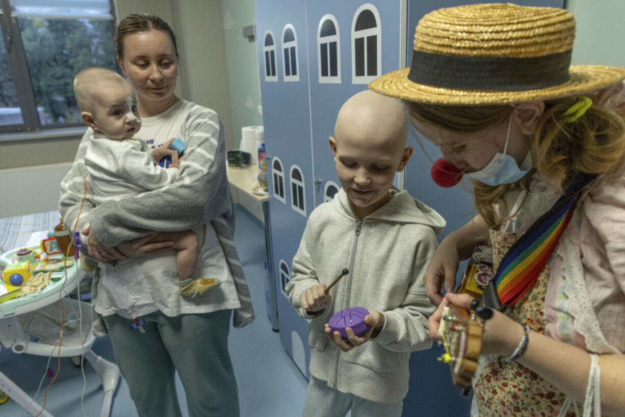 Tetiana Nosova, who goes by the clown name of Zhuzha, a volunteer from the &quot;Bureau of Smiles and Support&quot; plays a ukulele as she stands with Michael Bilyk, who is held by his mother Antonina Malyshko, and Kira Vertetska, 8, at Okhmatdyt children&#039;s hospital in Kyiv, Ukraine, Thursday Sept. 19, 2024.