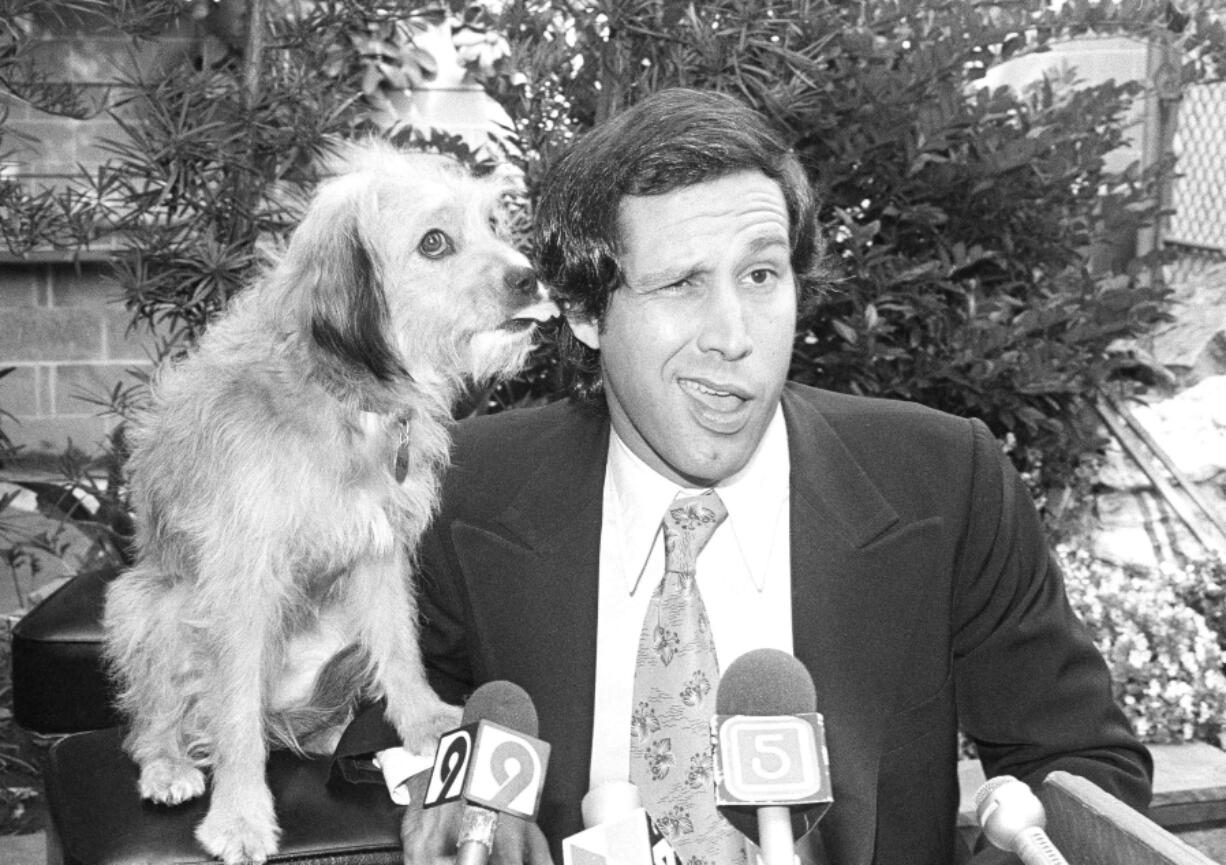 FILE -  Chevy Chase gets his ear licked from co-star Benji the dog, during a news conference in Los Angeles announcing their movie &ldquo;Oh Heavenly Dog&rdquo; on Sept. 6, 1979.