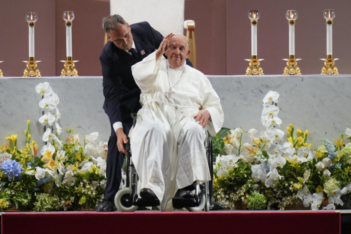 Pope Francis is helped by an aide to sit in the wheelchair after presiding over a holy mass at the SportsHub National Stadium in Singapore, Thursday, Sept. 12, 2024.