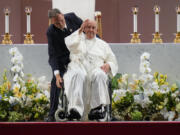 Pope Francis is helped by an aide to sit in the wheelchair after presiding over a holy mass at the SportsHub National Stadium in Singapore, Thursday, Sept. 12, 2024.