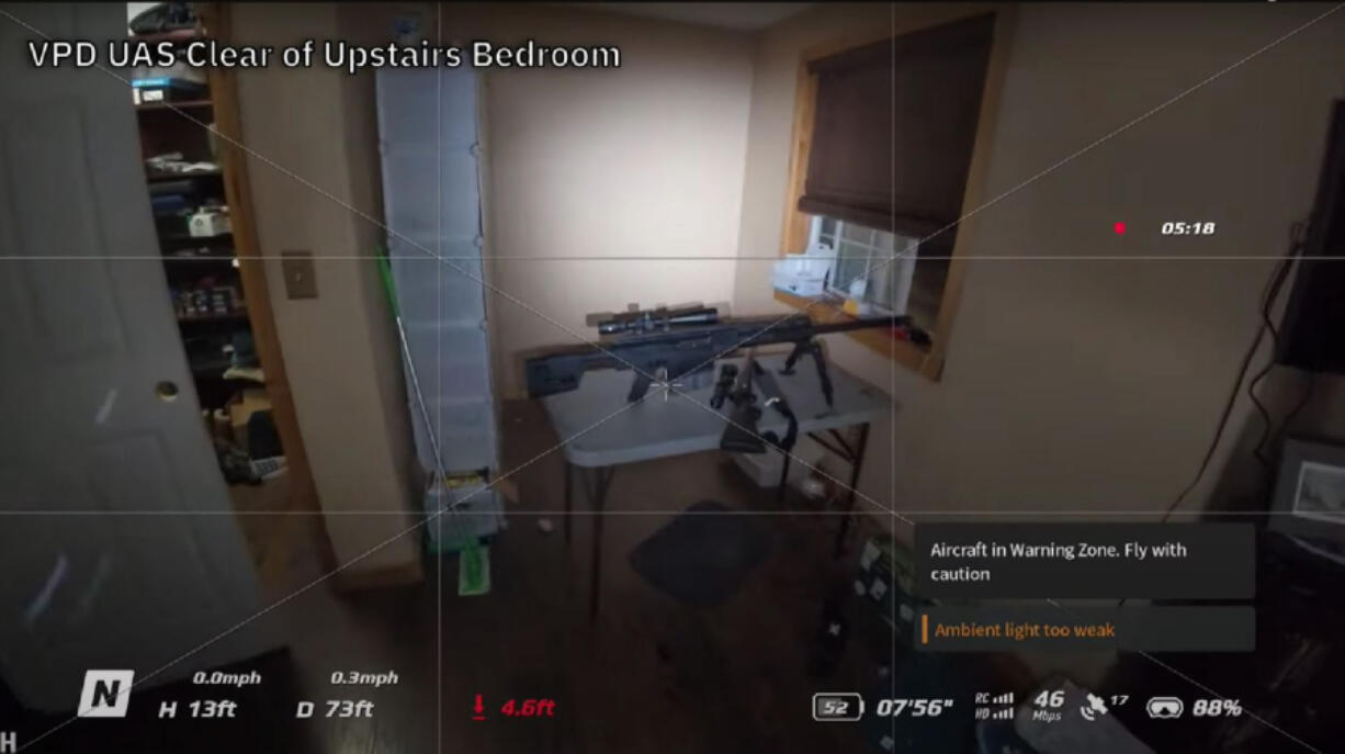 A screenshot from drone footage shows a rifle set up on a table in an upstairs bedroom.